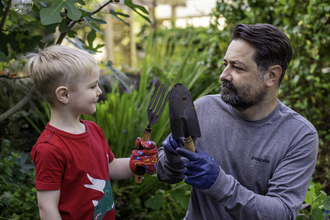 Man and young boy, looking at each other with small garden tools in their hands. Image by Evie and Tom Photography.